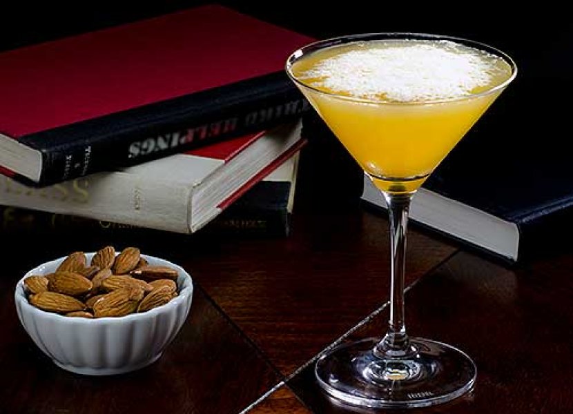 Cocktail and bowl of almonds in front of a stack of books