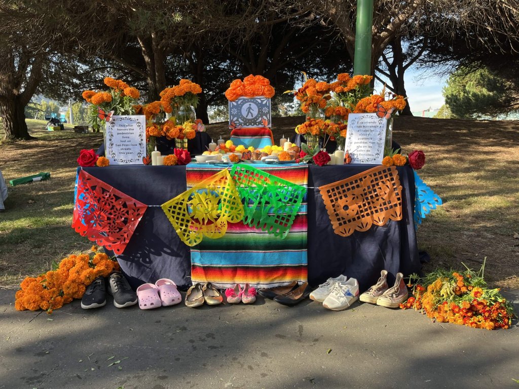 Day of the Dead altar with marigolds, shoes, and sign that honors lives lost in 2023 to traffic crashes.
