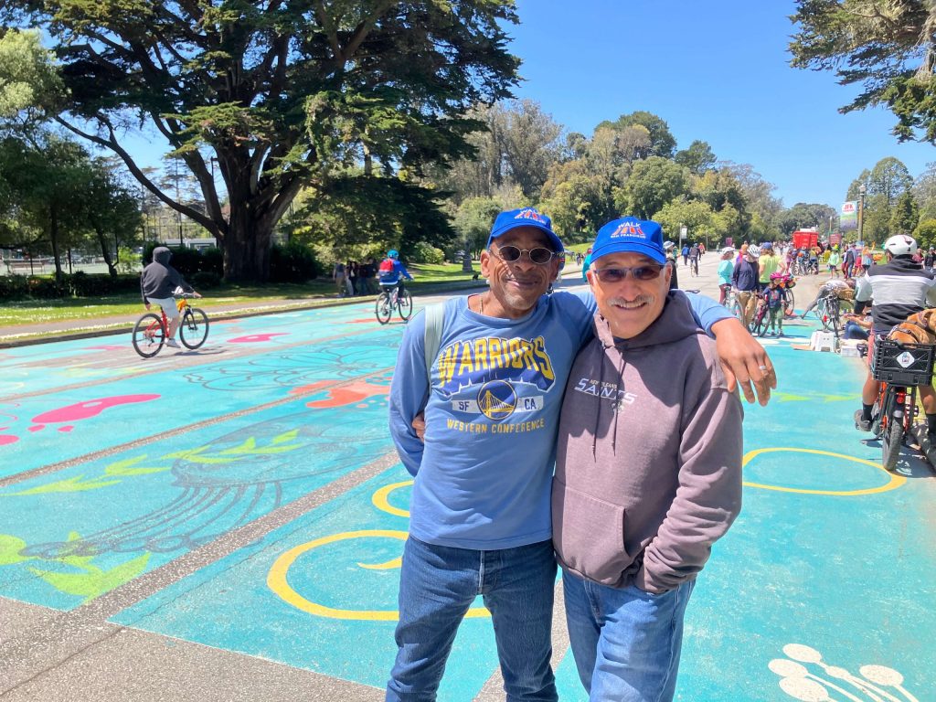 Two Walk SF members wearing Walk SF hats at the JFK Promenade's 4th Anniversary Community Picnic.