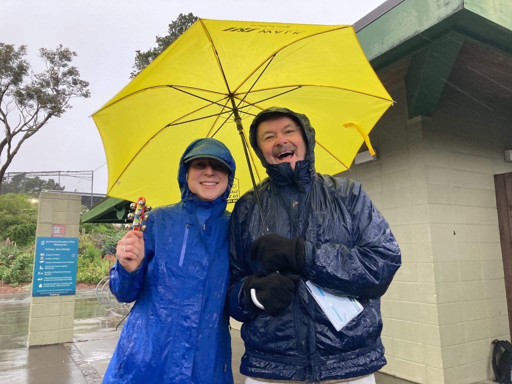 Two individuals pose for a picture under a bright yellow umbrella.