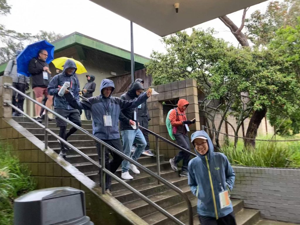 A group of people donning lanyards and raincoats walk down a flight of stairs.