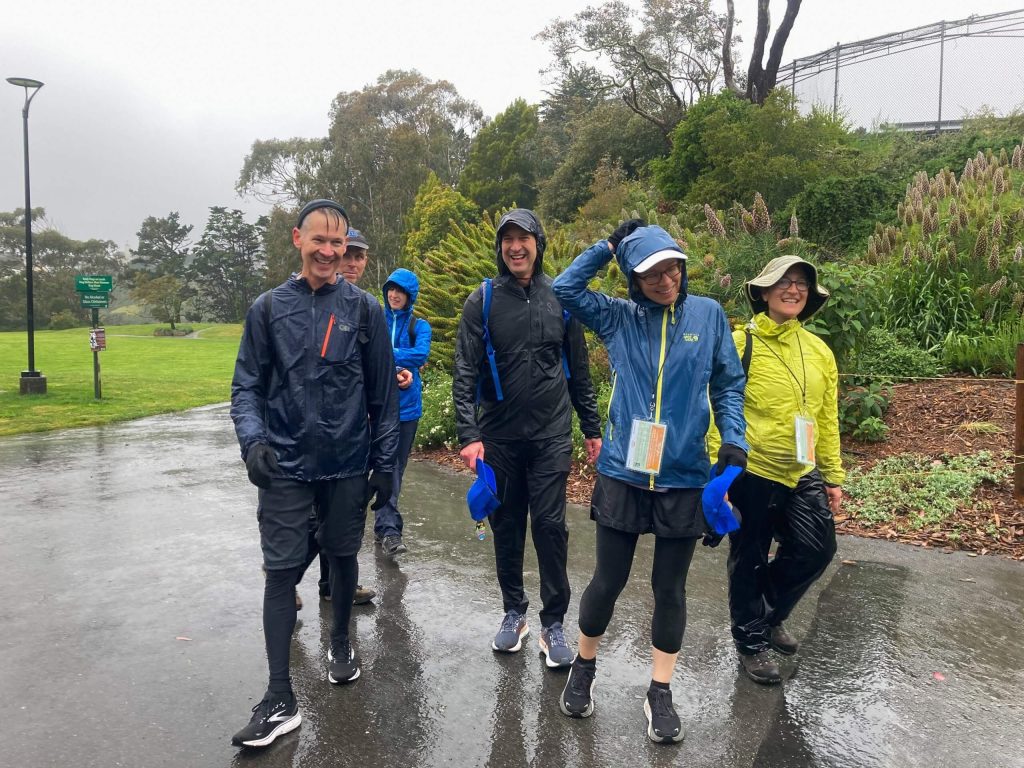 Six individuals walk along a paved path in the rain.