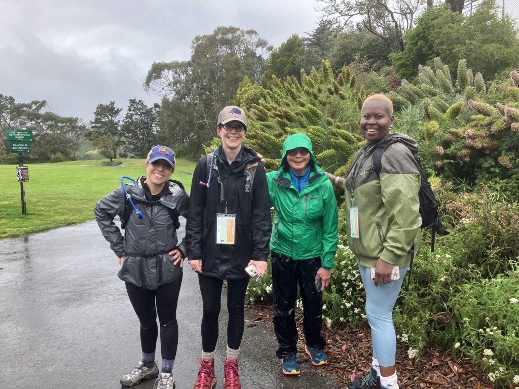 Four individuals pose on a paved path in front of some greenery.
