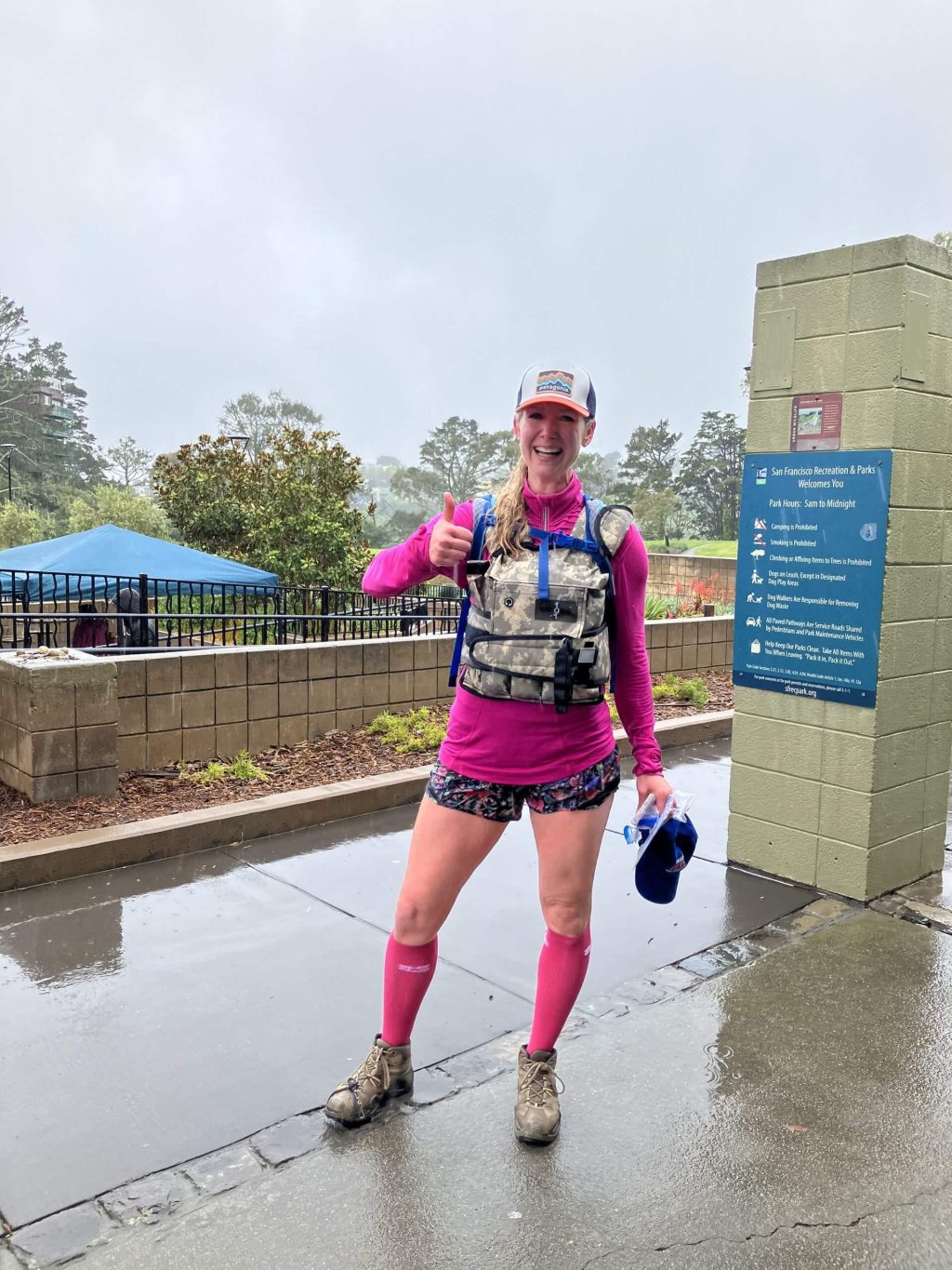 A woman wearing pink athletic gear gives a thumbs-up to the camera.